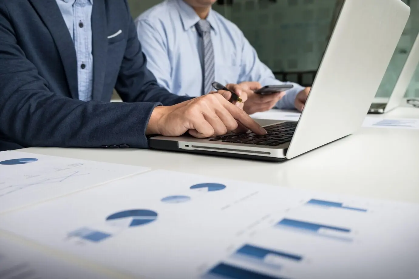 Процесс командной работы: молодые бизнес-менеджеры работают над новым стартап-проектом. На деревянном столе — ноутбук; печатают на клавиатуре, отправляют сообщения, анализируют графики и планы.