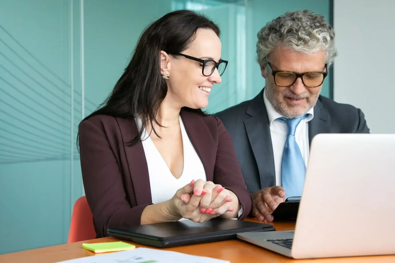 Жизнерадостные коллеги или деловые партнеры встречаются и обсуждают проект, сидят за открытым ноутбуком, используют планшет, разговаривают и улыбаются.